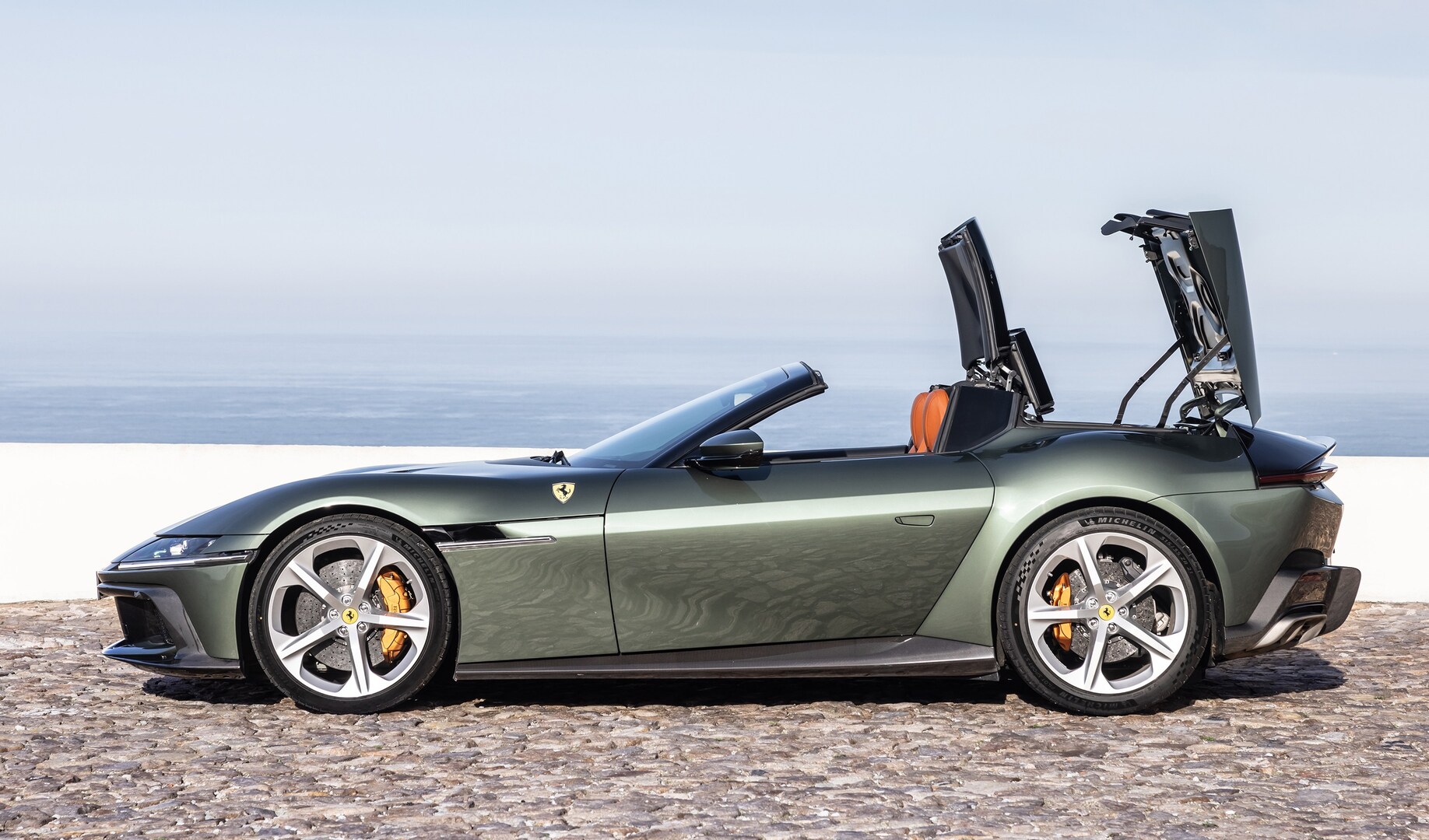 A green Ferrari Roma Spyder with its top up, parked near the ocean.