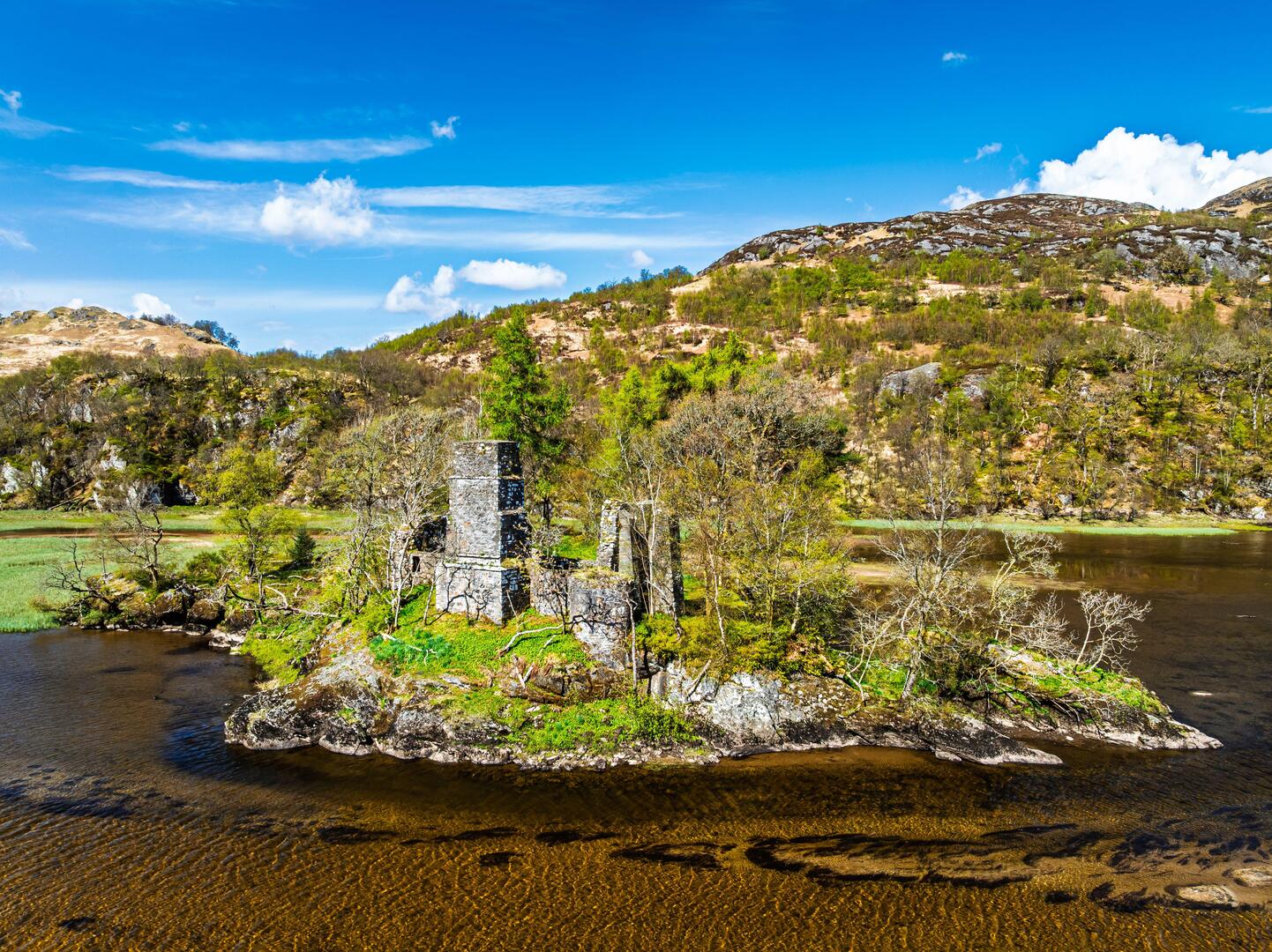 Aerial view of a ruined stone structure on a small island in a loch.