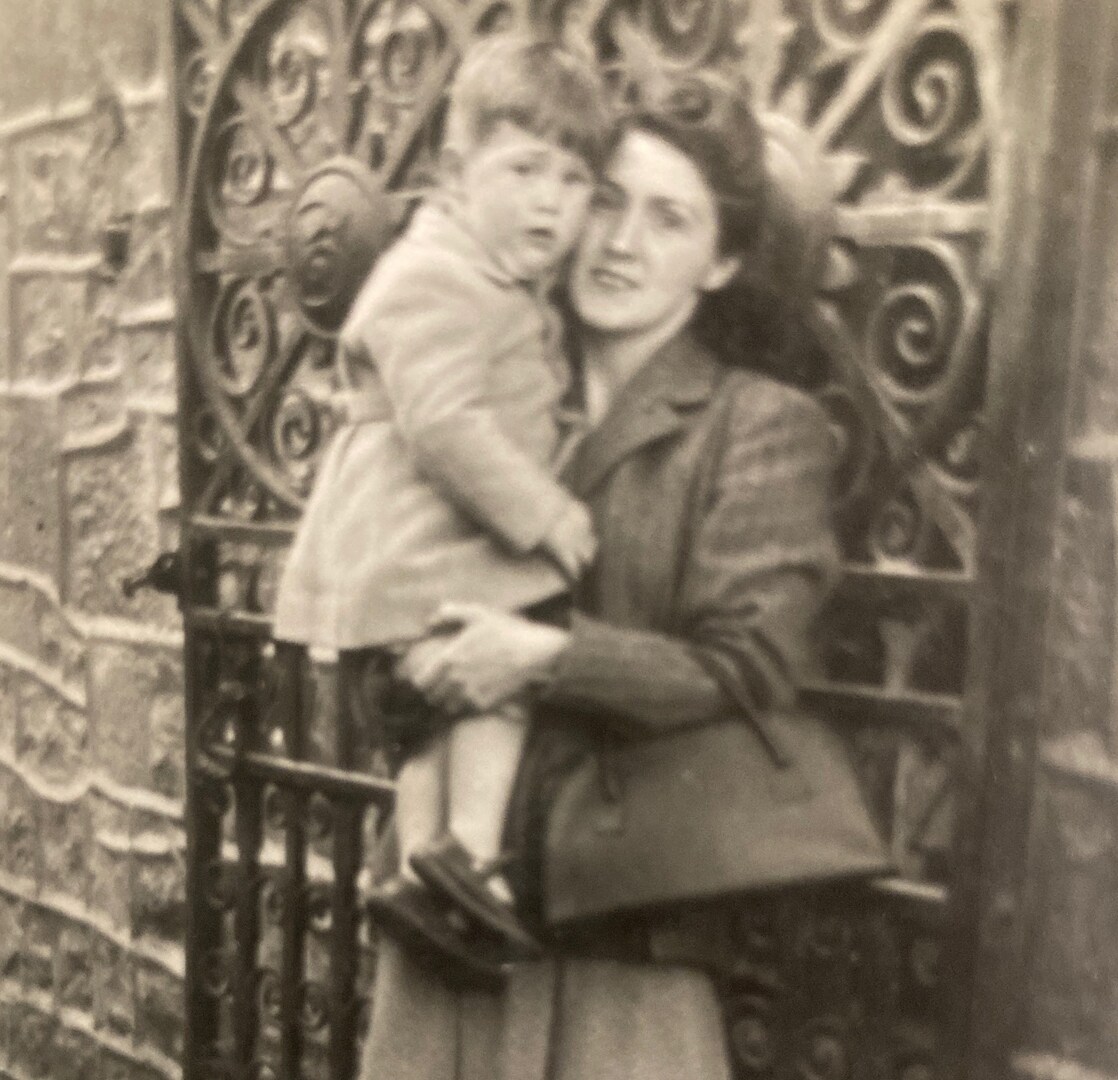Black and white photo of a woman holding a young child in front of a gate.