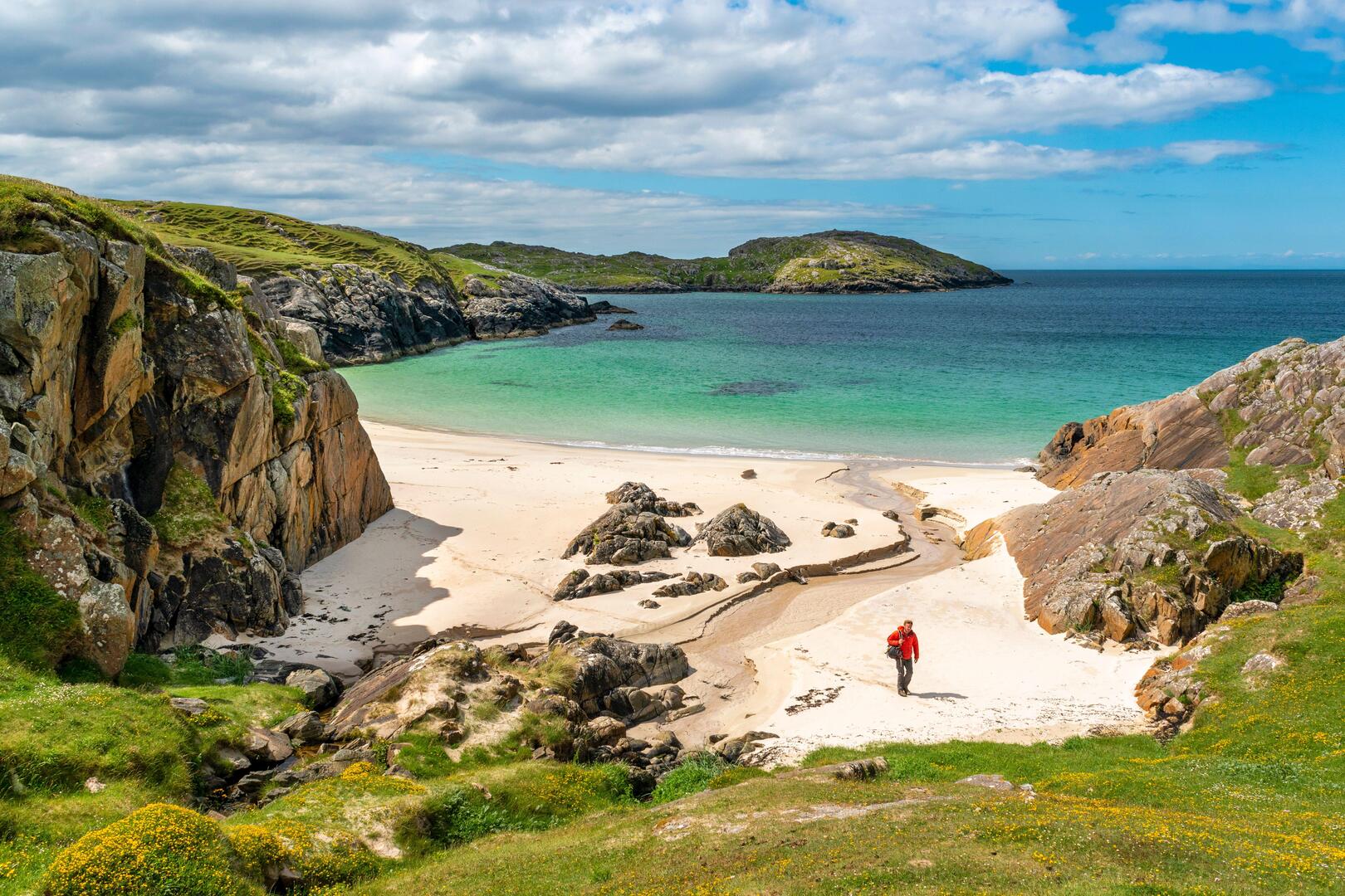 A lone hiker walks on Achmelvich Bay beach in Scotland.